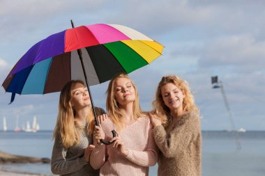 Renkli şemsiye altında üç güzel bayan arkadaş. Süveter giyen şık kadınlar dışarıda vakit geçiriyorlar..