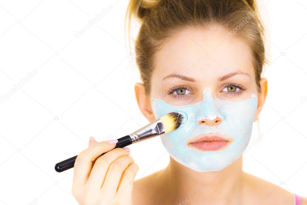 Young woman applying with brush green mud mask to face, on white. Teen girl taking care of oily skin, purifying the pores. Beauty treatment. Skincare.