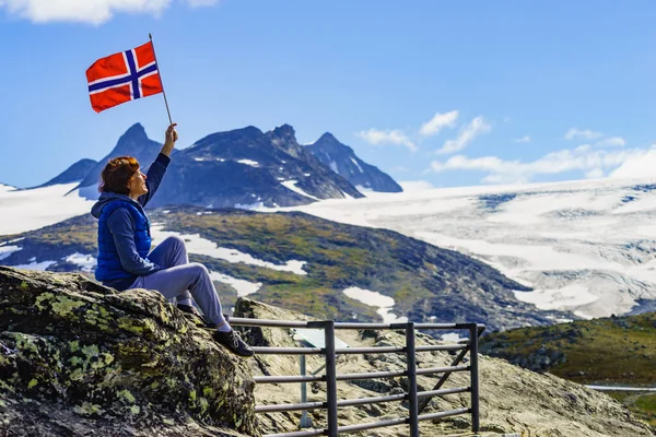 stock image Tourist woman enjoy mountains landscape, holding norwegian flag. National tourist scenic route 55 Sognefjellet, Norway