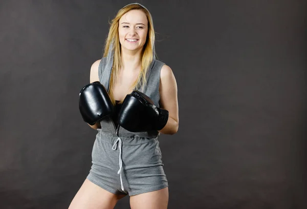 Young hooded woman fighting boxing. Blonde attractive girl wearing black punch gloves. Sport and fitness, power, exercising, on grey