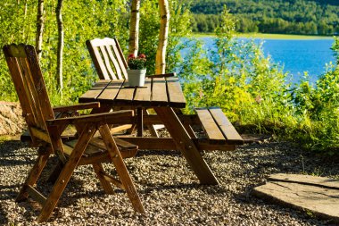 Piknik alanı dinlenme yeri ahşap sandalyeler ve Norveç gölü fiyort kıyısında çiçek süslemeli masa. Tatil tatilinde dinlenme. Avrupa İskandinavya.