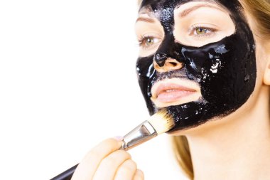 Siyah detoks detoks ile uygulanan genç bir kadın maskesini yüzüne doğru sıyırdı. Deriyle ilgilenen bir kız. Güzellik tedavisi. Cilt bakımı.