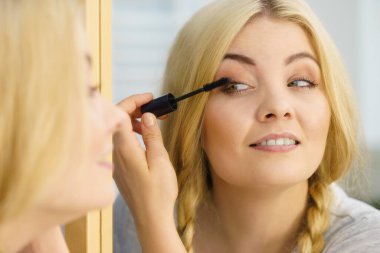 Makyajını siyah rimel sürerek yapan bir kadın kirpiklerini fırçalıyor. Kadın güzellik çehresi konsepti.