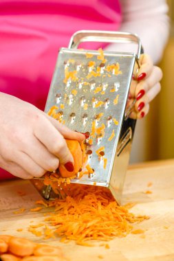 Tanınmayan bir kadın metal rende havuç rendeliyor, mutfak gereçleri sağlıklı sebze salatası hazırlıyor..