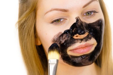Genç bir kadın yüzünde siyah detoks çamuruyla fırça kömür maskesi takıyor. Yağlı ciltle ilgilenen bir kız. Güzellik tedavisi. Cilt bakımı.