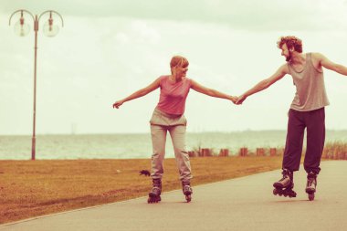 Aktif yaşam tarzı ve özgürlük kavramı. Deniz kıyısında paten süren genç ve zinde bir çift, kadın ve erkek birlikte vakit geçiriyorlar..