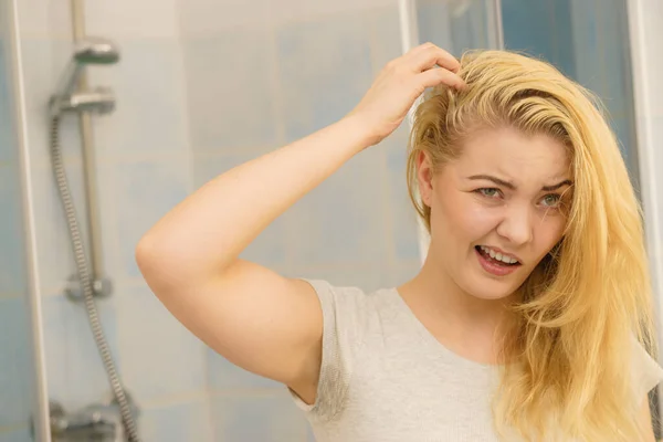 ブロンドの女性は バスルームで自分自身を見て脂っこい油性の髪に問題があります 頭皮を剥がしたり頭皮を剥がしたり — ストック写真