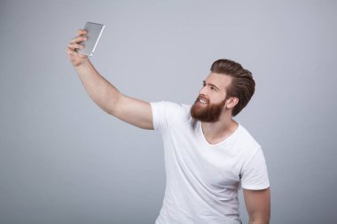 Sakallı yakışıklı genç selfie yapma ve gülümseyerek. O beyaz t tiþörtü