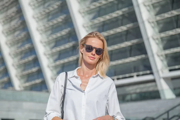 Business woman in a white shirt crossed her arms over her chest against of modern building. Dressed in a white shirt