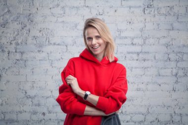 Tuğla duvar tarafından kırmızı kazak giyen çapraz silahlarla duran güzel genç gülümseyen kadın.