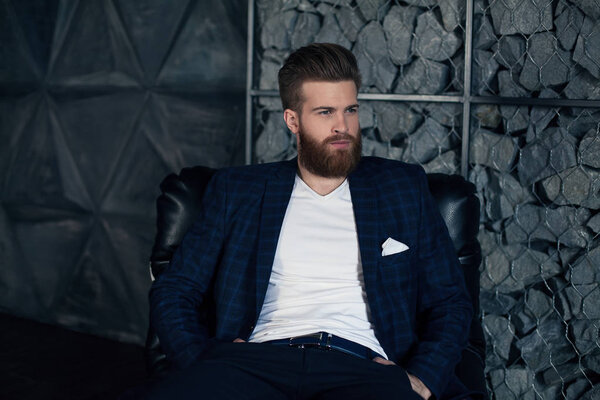 Thoughtful young modern man sitting at armchair.