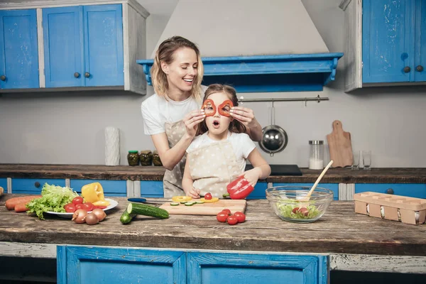 Eine schöne junge Mutter und ihre Tochter haben Spaß bei der Zubereitung ihrer Mahlzeit vor der blauen Küche — Stockfoto