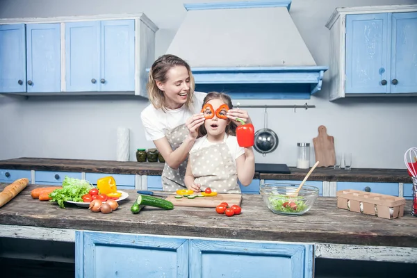 Eine schöne junge Mutter und ihre Tochter haben Spaß bei der Zubereitung ihrer Mahlzeit vor der blauen Küche — Stockfoto