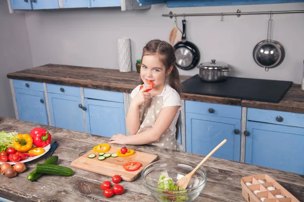 Ein nettes kleines Mädchen probiert bulgarischen Pfeffer vor einer schönen Küche — Stockfoto