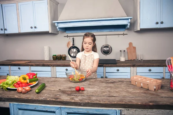 Eine kleine Tochter in der Küche mixt Salat mit einem großen Kochlöffel — Stockfoto