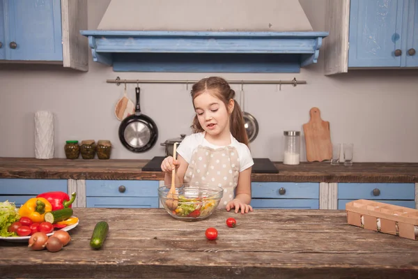 Eine kleine Tochter in der Küche mixt Salat mit einem großen Kochlöffel — Stockfoto