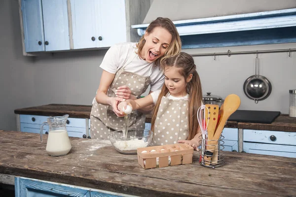 Mutter und Tochter in der Küche kochen Mafins. Tochter bricht das Ei über dem Mehl — Stockfoto