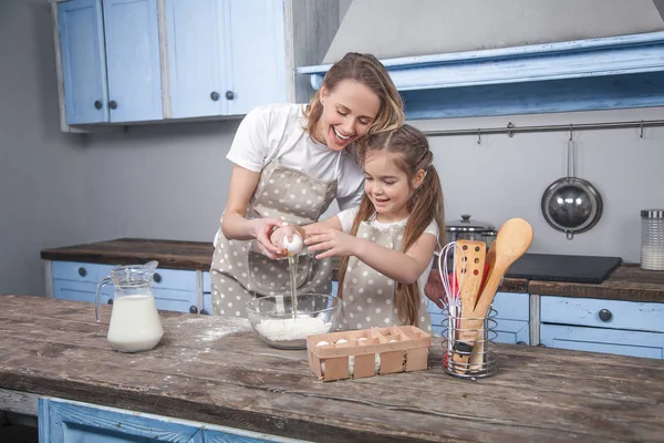 Mutter und Tochter in der Küche kochen Mafins. Tochter bricht das Ei über dem Mehl — Stockfoto