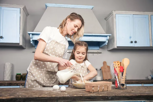 Mutter fügt Milch hinzu, während ihre Tochter Eier mit Mehl in der Schüssel vermischt. sie kochen mafins — Stockfoto