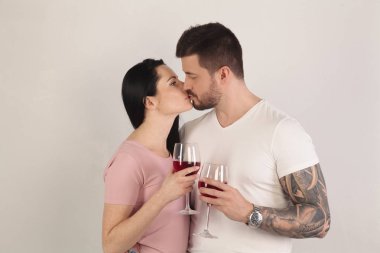 Güzel esmer çift İçecek şarap ve beyaz bir arka plan önünde öpüşme. Bir adam ile serin bir dövme elde