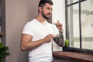 Genç yakışıklı düşünceli adam pencereye bakıyor ve onun sabah kahve sahip