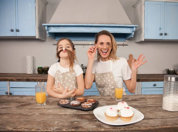 Glückliche liebevolle Familie in der Küche. Mutter und Tochter essen selbst gebackene Plätzchen und haben Spaß in der Küche, wo sie lustige Gesichter machen. Selbstgemachtes Essen, kleine Helfer — Stockfoto