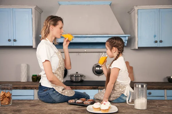 Glückliche liebevolle Familie in der Küche. Mutter und Tochter essen Kekse, die sie mit Orangensaft auf dem Küchentisch zubereitet haben — Stockfoto