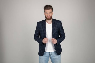 Bir ceket güzel seksi sakallı adam ceketini ellerini tutar ve kameraya bakar. o beyaz arka plan önünde duruyor