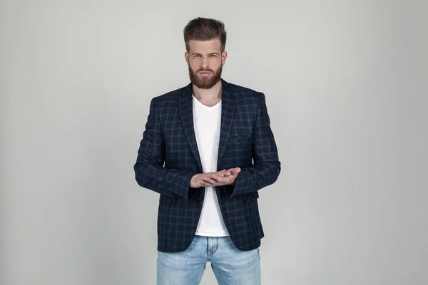 Un bel homme barbu sexy dans une veste tient ses mains croisées et regarde attentivement la caméra. il se tient devant le fond blanc — Photo