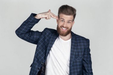 güzel bir saç stili ile sakallı adam. bir tabanca gibi başını elini tutar ve mizahi kendini öldürmek istiyor. iş yerinde sorunlar. Bir ceket koyun, beyaz arka plan önünde pozlar.