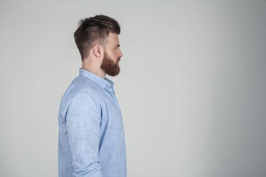 O profil beyaz bir arka plan önünde duruyor rahat giysiler giymiş güzel seksi sakallı adam