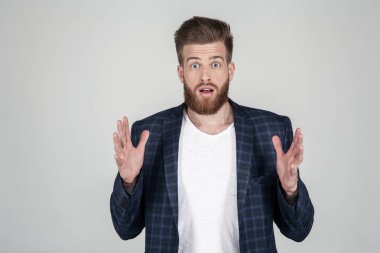 Güzel bir saç stili ile güzel seksi sakallı adam. kameraya bakarak korktu ve şaşırdı. Bir ceket giymiş, o beyaz arka plan önünde poz.
