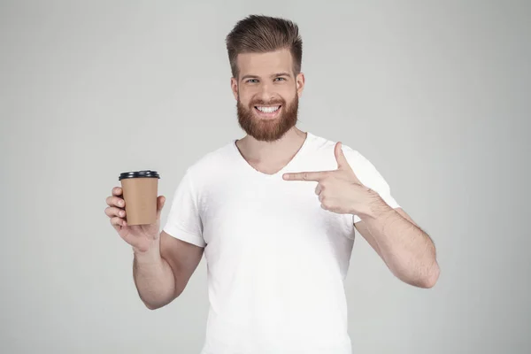 Portret pięknej seksownej Brodatego mężczyzny ubranego w białą koszulkę z ręką wskazuje na filiżankę kawy uśmiechniętej. stoi przed białym tłem — Zdjęcie stockowe