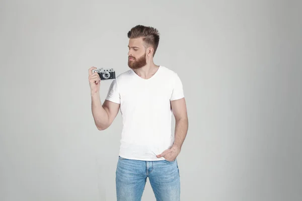 Retrato de un hermoso hipster sexy vestido con una camiseta blanca. sostiene en las manos de una vieja cámara, se para frente a un fondo blanco —  Fotos de Stock