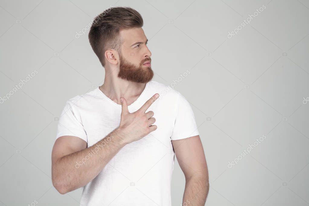 Attractive ginger male has thick beard, dressed in casual outfit, has serious expression, points with index finger at upper right corner