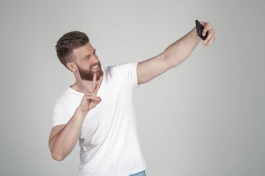 Gür zencefil sakallı memnun bir adam. Bir sephi yapar ve elV-işareti, iki parmaklı selam ile gösterir. Beyaz bir tişört ve kot pantolon giyiyor. beyaz arka planın önünde durmak