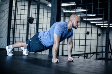 Strength and motivation. Side view of young handsome bald man in sportswear doing push-up at gym