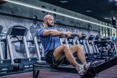 Fitness kulübünde kürek makinesi kullanan erkek. Genç adam spor salonunda fitness makinesi egzersizleri yapıyor. Yan görünüm