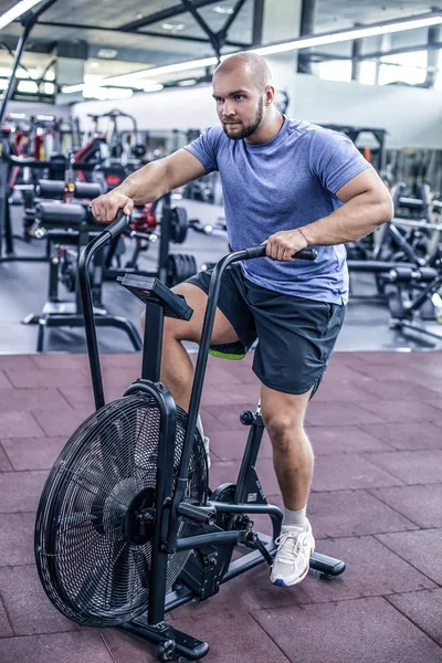 Jeune homme utilisant vélo d'appartement à la salle de gym. Fitness mâle utilisant un vélo pneumatique pour l'entraînement cardio à la salle de gym Crossfit . — Photo