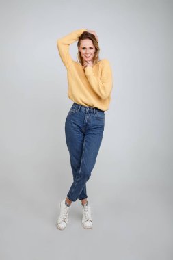 şık giysiler giymiş güzel bir sarışın, tam uzunlukta bir portre. Bir eliyle saçını tutar, diğer eliyle çenesini tutar. beyaz arka plan önünde pozlar