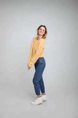 Oynamak ve gülümsemek. Şık giysiler giymiş güzel bir sarışın, tam uzunlukta bir portre. beyaz arka plan önünde pozlar