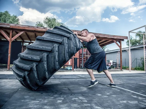 Vue latérale d'un homme de fitness musclé en mouvement gros pneu dans la salle de gym de rue. Levage de concept, entraînement — Photo
