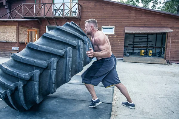 Tire flip exercise. Sportsman is engaged in workout with heavy tire in street gym. Concept lifting, workout training — Stock Photo, Image