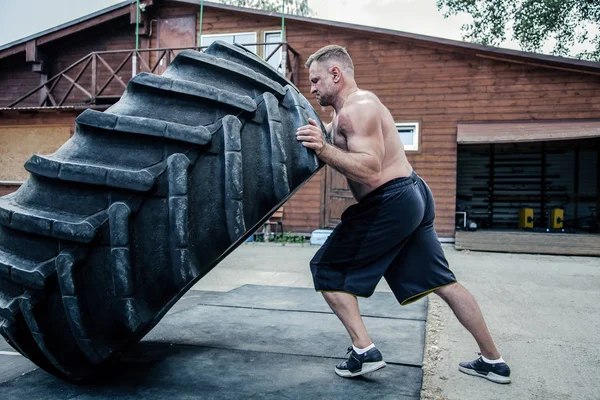 Side view of strong muscular fitness man moving large tire in street gym. Concept lifting, workout training — Stock Photo, Image