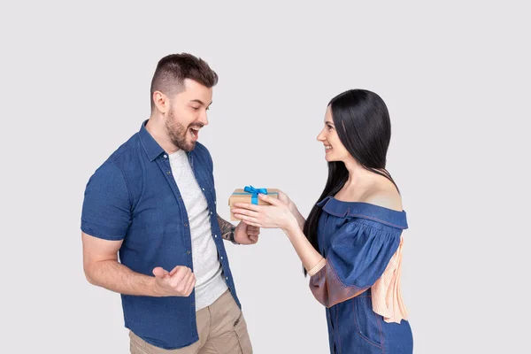 Jolie femme surprenant son petit ami avec cadeau isolé portant des vêtements en denim sur fond gris cendré — Photo