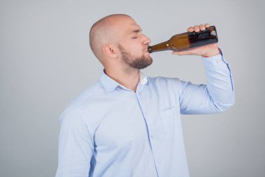 Profilde duran ve işten sonra bira içen bir adamın portresi. beyaz arka plan üzerinde izole bir gömlek giymiş