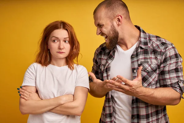 Furious bearded guy screams and gestures angrily, yells at woman, have dispute, pose together over yellow background. Strict boss being angry with not responsible colleague.