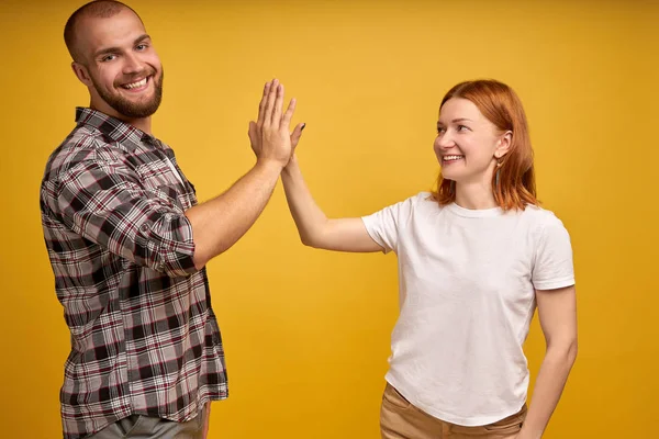 Image de jeunes gens sympathiques homme et femme en vêtements de base riant et donnant haute cinq isolé sur fond jaune — Photo