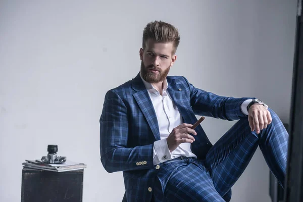 Guapo hombre barbudo seguro está sosteniendo un cigarro, mirando a la cámara — Foto de Stock