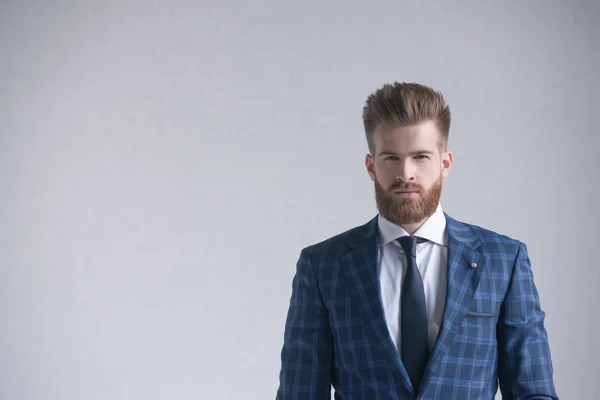 Elegante hombre de negocios barbudo guapo mirando cámara aislada en gris. Inthe left es un espacio libre para su logotipo o texto — Foto de Stock